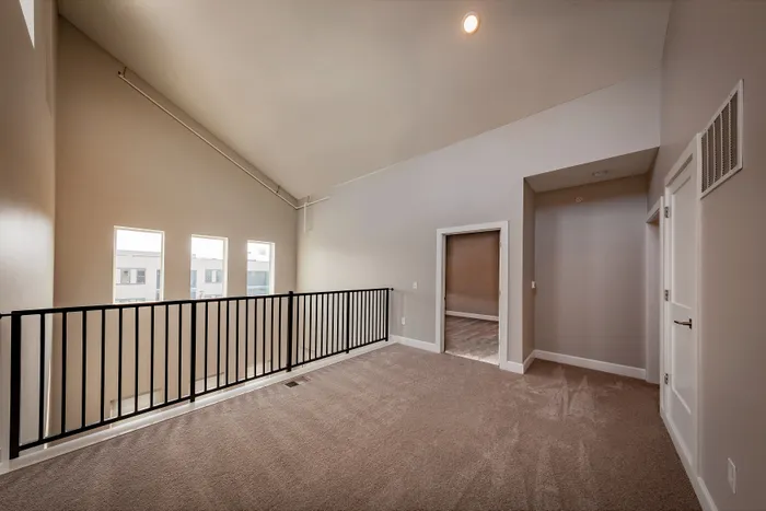 Modern loft space with vaulted ceilings, plush carpet, and sleek railing overlooking sunlit windows.