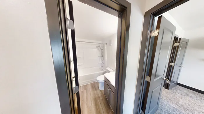 Modern bathroom featuring sleek wooden flooring, elegant dark trim, and a bright, spacious layout with a bathtub and vanity.