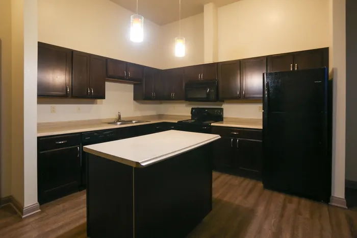 Modern kitchen with dark wood cabinets, sleek countertops, and a spacious island illuminated by stylish pendant lights.