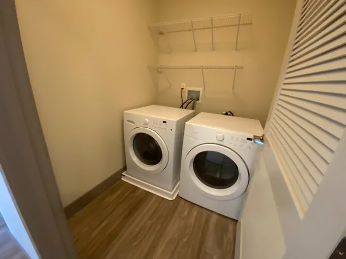 Convenient in-unit laundry room featuring modern washer and dryer with ample shelving for storage.