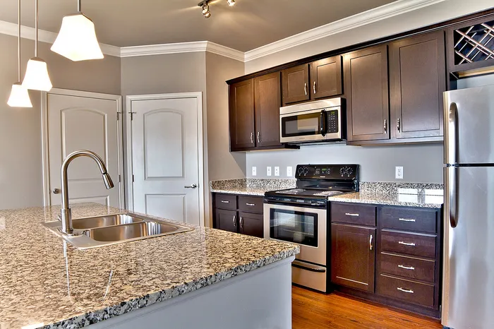 Modern kitchen with elegant granite countertops, dark wood cabinetry, and stainless steel appliances under soft pendant lighting.
