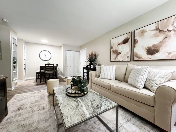 Elegant living room featuring a plush beige sofa, modern marble-topped coffee table, and artistic wall decor, complemented by a cozy dining area with stylish wooden furniture.