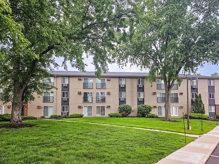 Charming apartment complex façade with lush green landscaping and mature trees offering a serene and inviting atmosphere.
