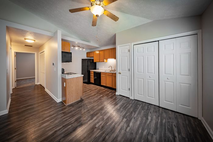 Bright, modern living space featuring elegant wooden flooring, open kitchen with sleek black appliances, and ample closet storage at Cypress Square Apartments in Lafayette, IN.
