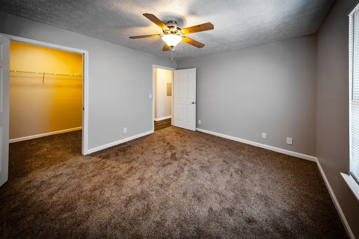 Spacious bedroom with plush carpet, ceiling fan, and ample natural light, featuring a large walk-in closet at Cypress Square Apartments in Lafayette, IN.