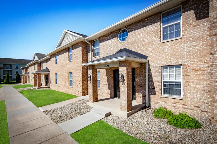 Charming brick apartment community with manicured green lawns and welcoming entrance, ideal for comfortable living.