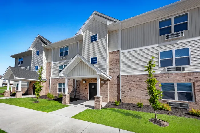 Modern apartment building with a welcoming entrance, fresh landscaping, and large windows.
