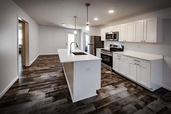 Modern kitchen with sleek white cabinetry, stainless steel appliances, and elegant pendant lighting over a spacious island. Rich wood flooring enhances the open, inviting space.