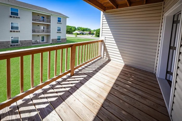 Sunlit balcony with wooden railing offering serene views of vibrant green lawns and modern apartment community.
