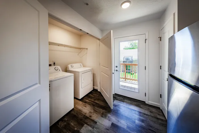 Bright laundry room featuring modern washer and dryer, elegant wood flooring, and a glass door leading to a sunlit balcony.