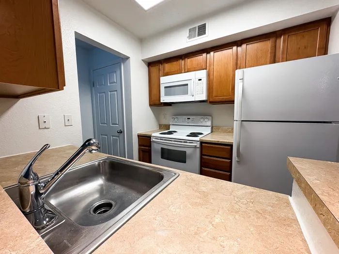 Modern kitchen with sleek stainless steel sink, white appliances, and warm wood cabinetry.