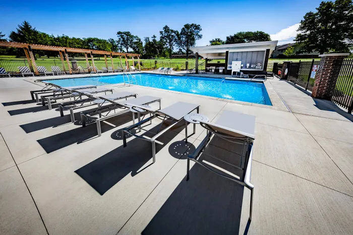 Luxurious outdoor pool area with modern sun loungers and a pergola, surrounded by lush greenery for a serene retreat.