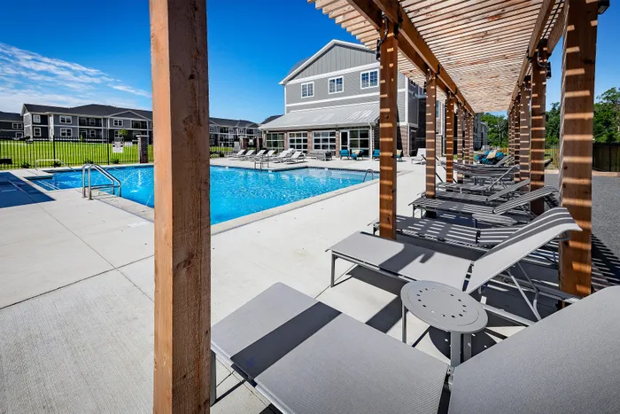 Luxurious apartment complex featuring a pristine swimming pool with elegant lounge chairs under a stylish pergola, ideal for relaxation and leisure.