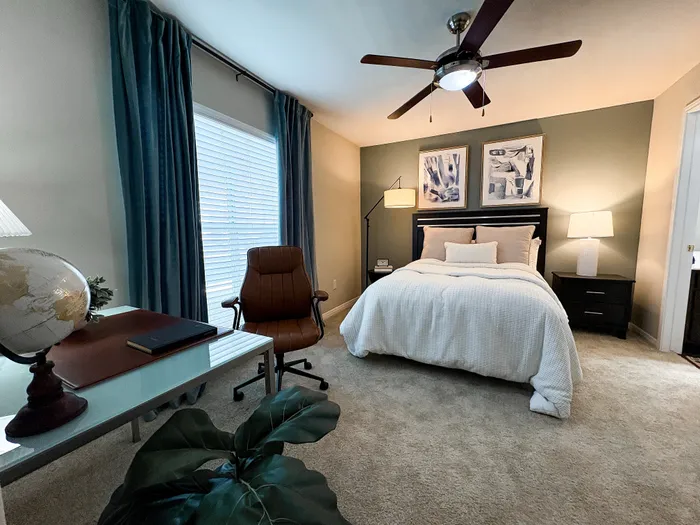 River Crossing bedroom with plush carpeting, elegant bedding, stylish decor, and a cozy workspace featuring a globe and modern chair.