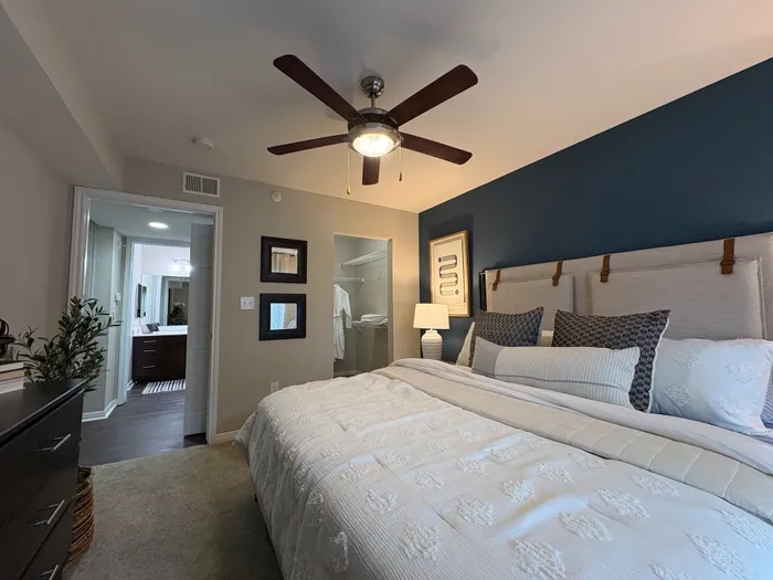 River Crossing elegant bedroom with modern design, featuring a cozy bed adorned with stylish cushions, a chic ceiling fan, and an inviting walk-in closet.