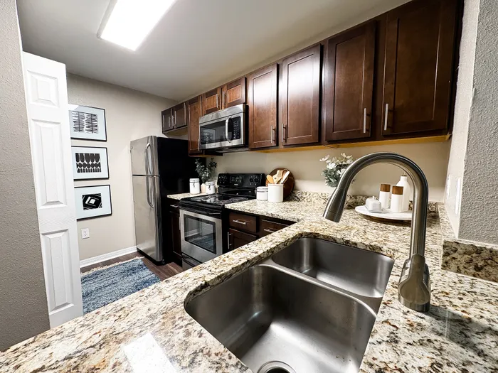 River Crossing modern kitchen with sleek granite countertops, stainless steel appliances, and rich wood cabinetry, complemented by elegant wall art.
