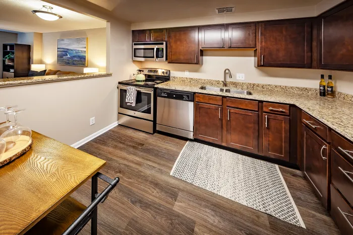 Elegant kitchen with warm wooden cabinetry, stainless steel appliances, and granite countertops. Open view into a cozy living space with modern decor.