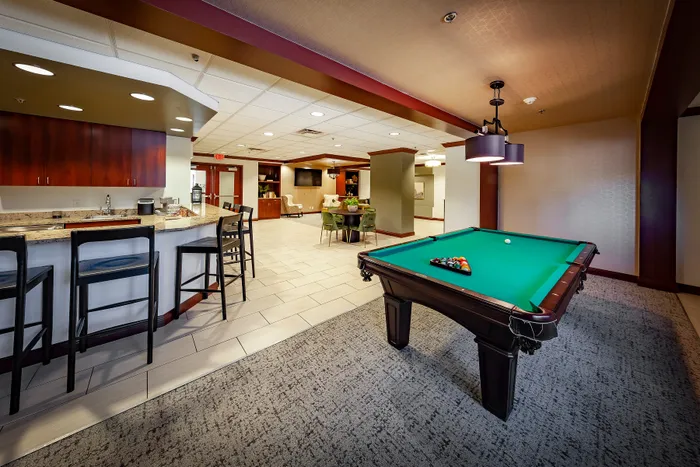 Luxurious apartment amenity area featuring a sleek billiards table, cozy dining space, and a modern bar with stylish seating.