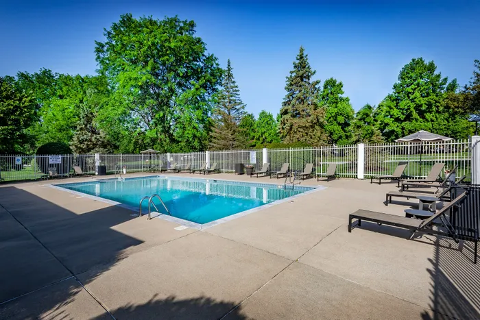 Inviting outdoor pool area with comfortable lounge chairs, surrounded by lush greenery and fenced for privacy.