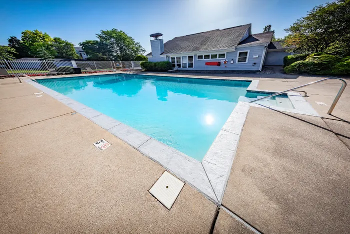 Inviting outdoor pool with clear blue water, surrounded by a clean patio and lush greenery, perfect for relaxation and leisure.
