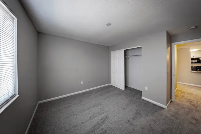 Inviting and spacious bedroom with plush carpet, large window for natural light, and ample closet space in a modern apartment.