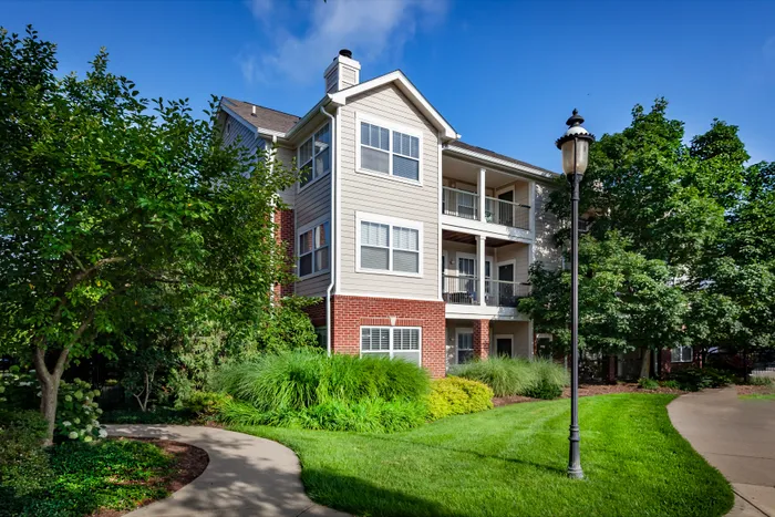 Charming apartment building with brick and siding exterior, surrounded by lush greenery and scenic walkways.