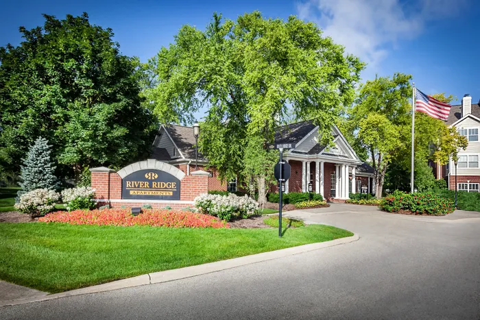 Charming River Ridge Apartments entrance with lush greenery, vibrant flower beds, and elegant brick architecture.