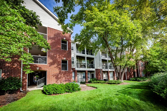 Charming apartment complex with elegant brick exterior, lush green landscaping, and inviting balconies under a clear blue sky.