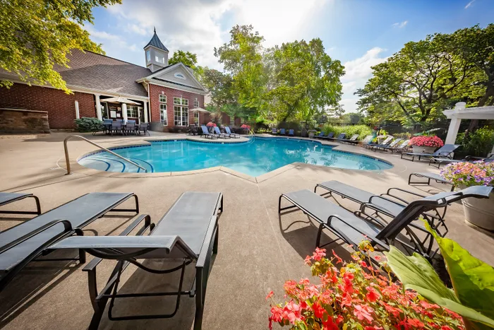 Inviting outdoor pool area with sun loungers, surrounded by lush greenery and blossoming flowers, perfect for relaxation and social gatherings.