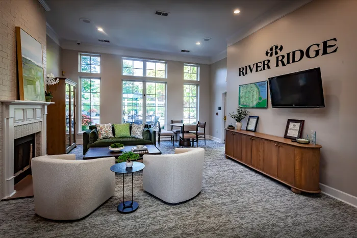 Inviting community lounge at River Ridge with plush seating, a cozy fireplace, and abundant natural light through large windows.