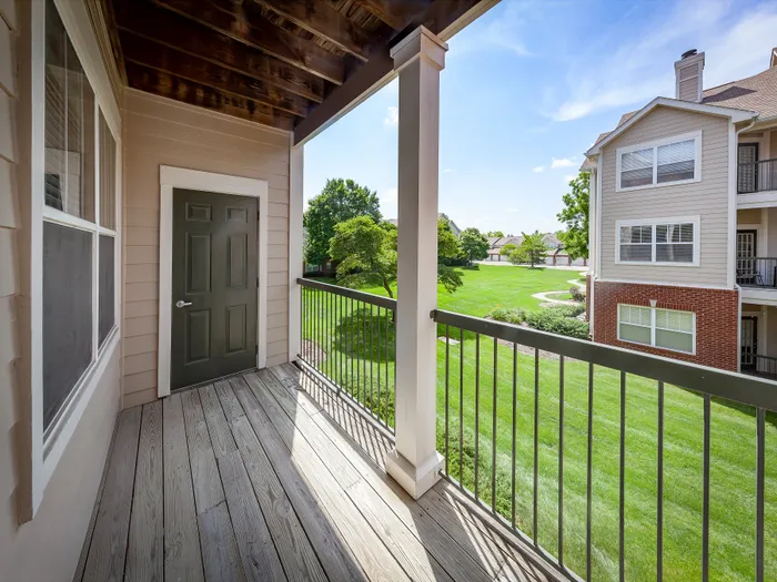 Inviting apartment balcony with wooden flooring overlooking a lush green courtyard, perfect for relaxation.