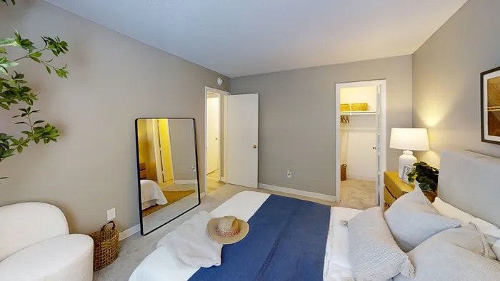 Pebble Point elegant bedroom with modern decor, featuring a cozy bed, a large mirror, and an inviting walk-in closet.