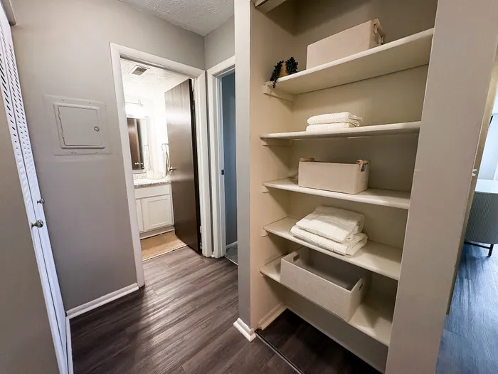 Inviting apartment hallway featuring stylish hardwood floors, well-organized open shelving, and a glimpse into a modern bathroom with elegant fixtures.