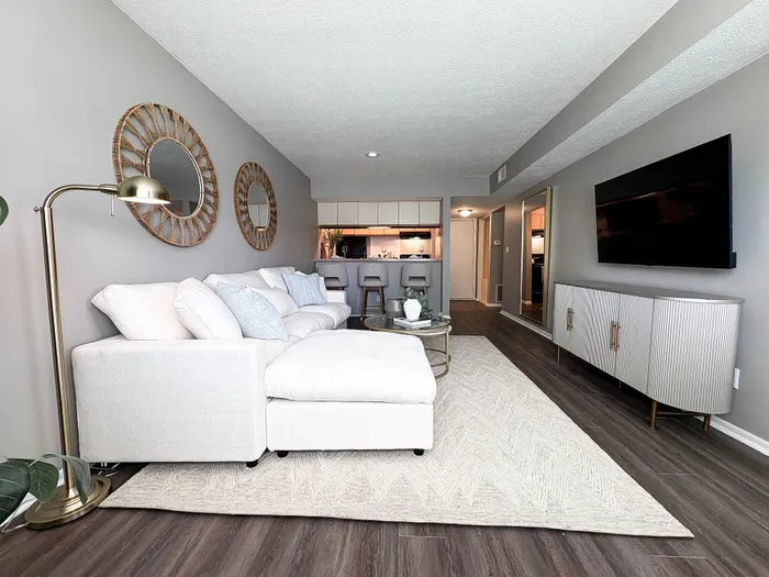 Inviting living room with a chic white sectional sofa, stylish mirrors, and sleek modern decor in an open-concept apartment.