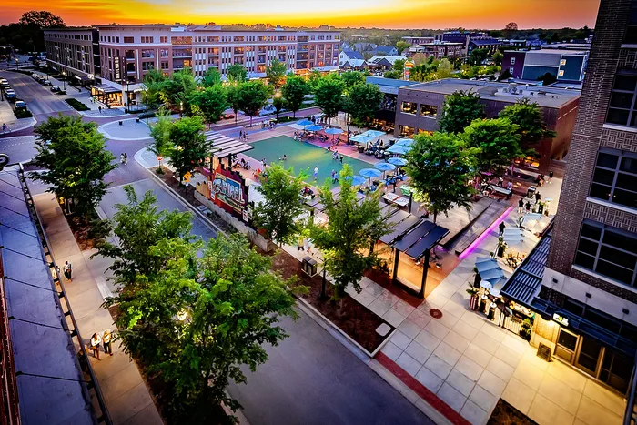 Railyard at Midtown Apartments - Vibrant urban plaza at sunset, featuring lively outdoor seating and lush trees, surrounded by modern architecture.