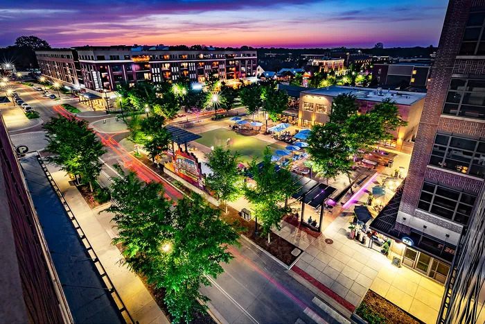 Railyard at Midtown Apartments - Vibrant urban plaza at sunset, featuring lively nightlife with illuminated streets and bustling outdoor dining areas.