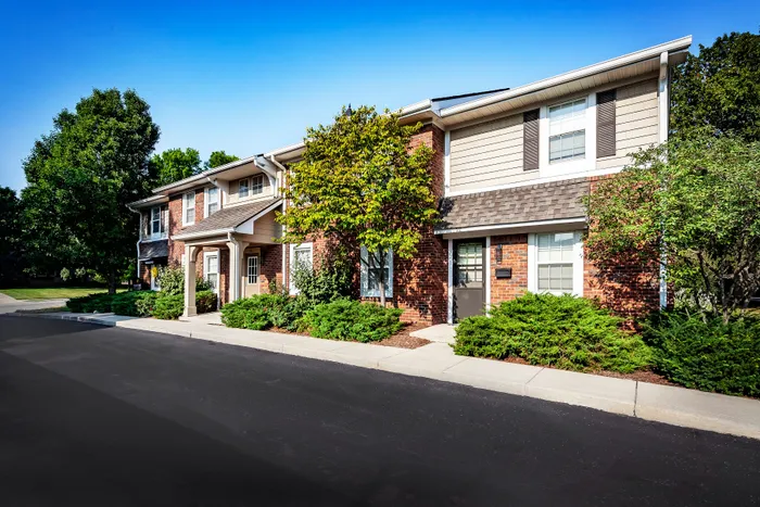 Main Street on the Monon Apartments - Charming row of brick townhouses with lush landscaping and clear blue skies, offering a serene suburban ambiance.