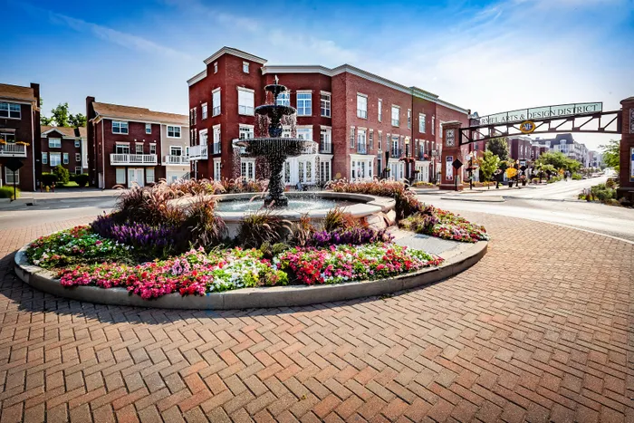 Vibrant streetscape in Carmel Arts & Design District featuring a classic fountain with colorful flower beds, surrounded by charming red brick buildings.