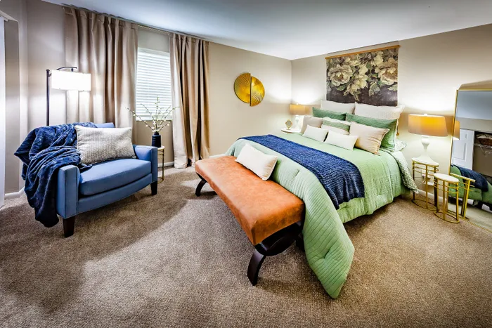 Main Street on the Monon Apartments - Inviting bedroom with plush green bedding, elegant lighting, and cozy blue armchair creating a relaxing ambiance.