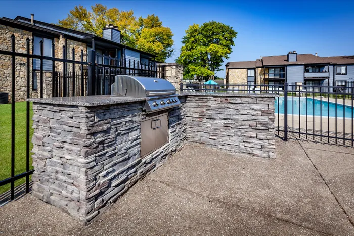 Pebble Point Apartments - Beautiful apartment complex featuring a stylish outdoor grill area with stone detailing beside a refreshing swimming pool surrounded by lush trees.