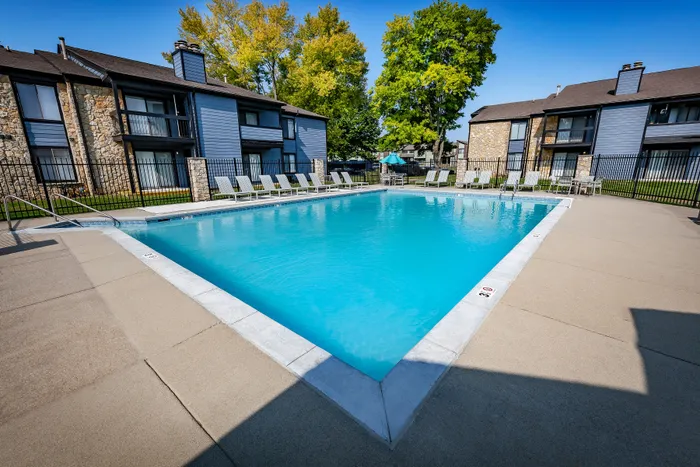 Pebble Point Apartments - Inviting outdoor pool area with modern lounge chairs, surrounded by charming apartment buildings and lush greenery.