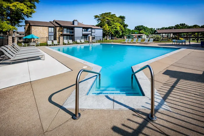 Pebble Point Apartments - Outdoor pool area with modern lounge chairs, surrounded by lush greenery and elegant apartment buildings.
