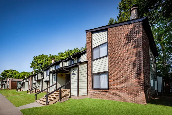 Pebble Point Apartments - Charming two-story apartment buildings with brick and siding exteriors, surrounded by lush greenery.