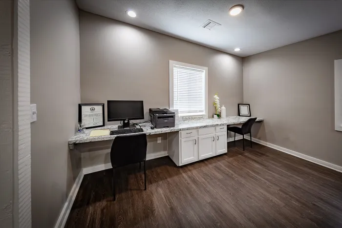 Pebble Point Apartments - Modern business center with sleek granite desk, computer, and printer, accented by soft lighting and elegant white cabinetry.