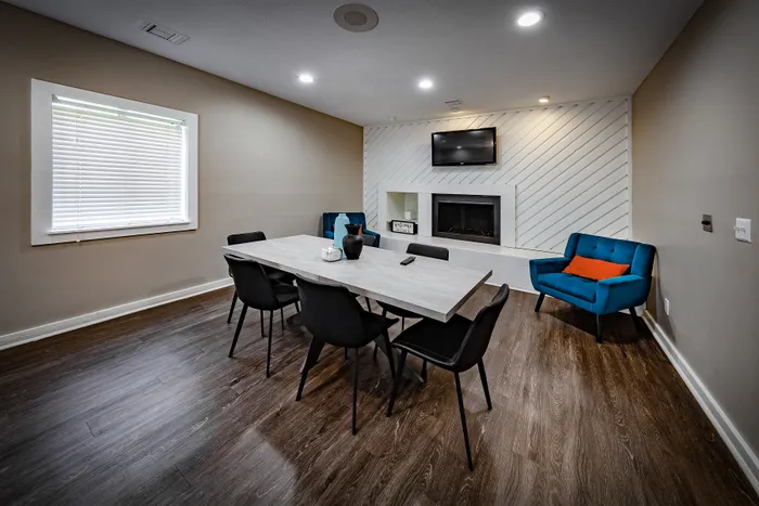 Pebble Point Apartments - Modern dining area in the clubhouse with a sleek table, six black chairs, vibrant blue armchair, and stylish fireplace, ideal for cozy gatherings.