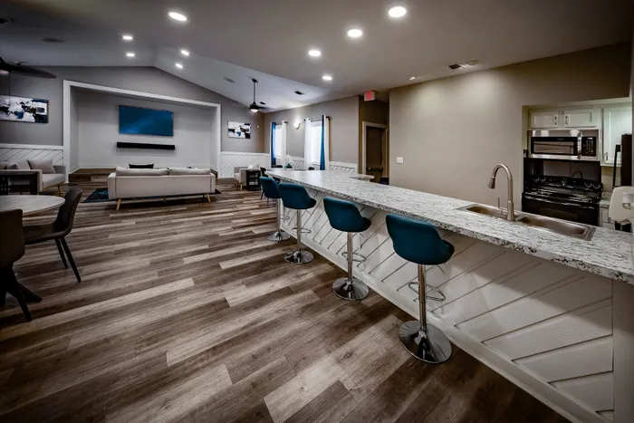 Pebble Point Apartments - Modern open-concept leasing office space featuring a sleek kitchen with a granite countertop bar, comfortable seating area, and stylish wood flooring.
