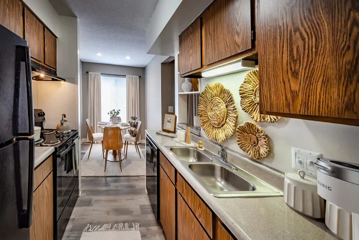 Pebble Point Apartments - Chic apartment kitchen with warm wooden cabinets, modern appliances, and a cozy dining area adorned with natural light and artistic wall decor.