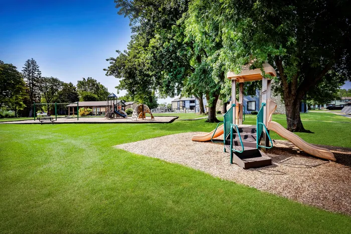 Pebble Point Apartments - Charming residential playground with modern equipment surrounded by lush greenery and shaded picnic areas.