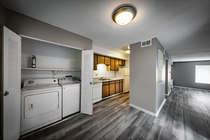 Pebble Point Apartments - Modern apartment with open-concept kitchen, stylish wood cabinetry, and convenient in-unit laundry. Spacious living area with contemporary flooring and ample natural light.