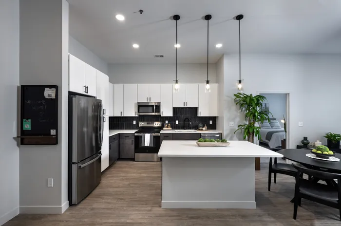 The Elex Apartments - Modern open-concept kitchen with sleek black and white cabinetry, elegant pendant lighting, and spacious island counter, ideal for entertaining and culinary creativity.